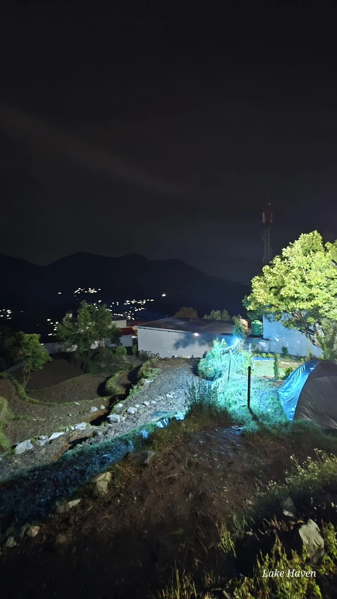 Night view near Sari Village with a tent, trees and distant mountain village lights